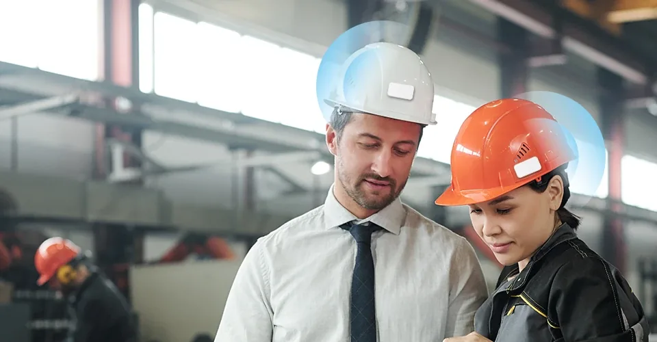A supervisor and a worker in hard hats fitted with beacon tags on a factory floor